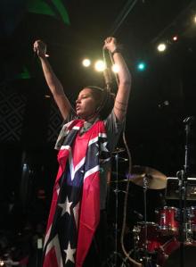 This April 26, 2016 photo provided by Genesis Be, a rapper who grew up in Biloxi, Miss., shows her draped in a Confederate battle flag and holding a noose around her neck during a performance at the music venue "SOB's" in New York. The musician was protesting Mississippi Gov. Phil Bryant's proclamation of April as Confederate Heritage Month. (Robin Hodgson/Genesis Be Productions via AP)