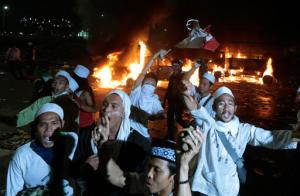 Muslim protesters chant slogans near burning police trucks during a clash with the police outside the presidential palace in Jakarta, Indonesia, Friday, Nov. 4, 2016. Police in the Indonesian capital clashed with hard-line Muslim protesters refusing to disperse after a massive protest Friday to demand the arrest of the city's minority-Christian governor for alleged blasphemy. (AP Photo/Dita Alangkara)